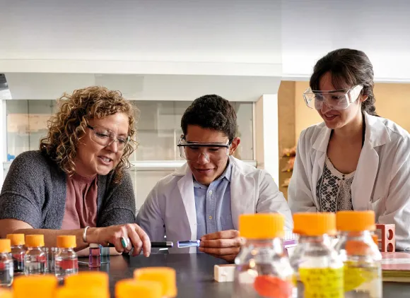 Three scientists wearing safety glasses in a lab with test bottles in the foreground