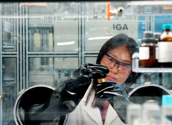 A researcher in a lab coat manipulates samples in an enclosed glove box.