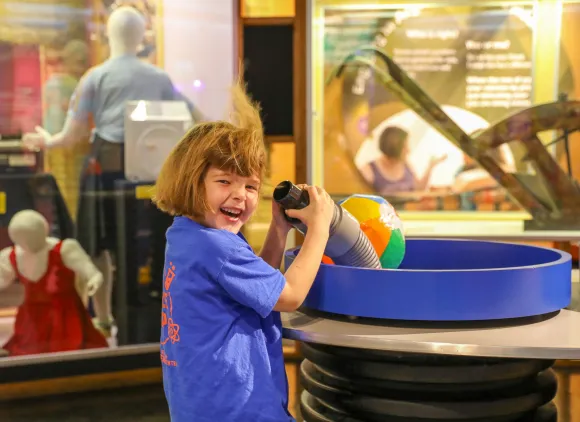 A young girl in a museum laughs as air blowing from a tube whips up her hair.