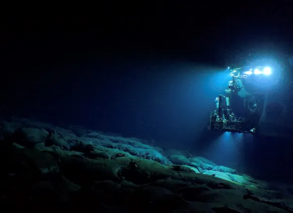 Underwater view of the Alvin submersible lit brightly in dark blue water.