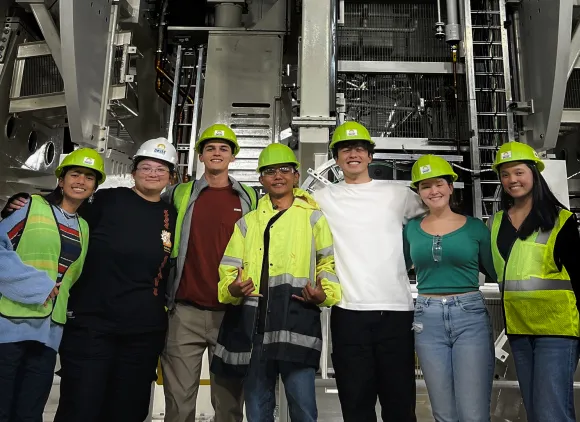 Group photo of students and mentors wearing hard hats in front of interior workings of the Inouye Solar Telescope facility