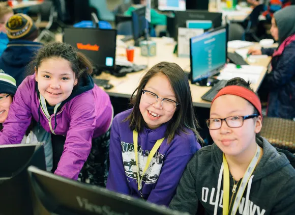 Four smiling kids behind computers.