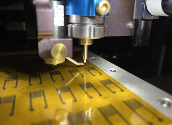 An aerosol jet printer in Mark Hersam's Northwestern University laboratory deposits electronic inks onto a flexible polymer substrate. The printed artificial neurons can generate realistic brain-like signals that activate living neurons. The device uses flexible, low-cost electronic inks instead of rigid silicon fabrication. The approach could lead to bioelectronics that communicate directly with the brain and energy-efficient, brain-inspired computing.