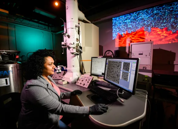 A researcher sits at a computer in a darkened lab.