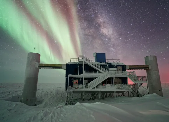 A building with steps and columns, surrounded by snow and with the Milky Way and auroras appearing in the background.