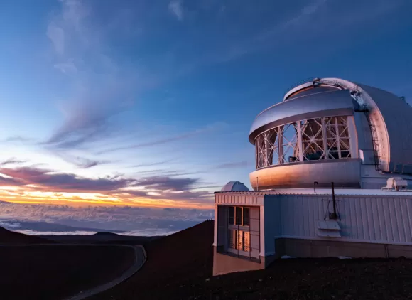 Gemini North Observatory telescope against a blue sky with clouds at dusk.