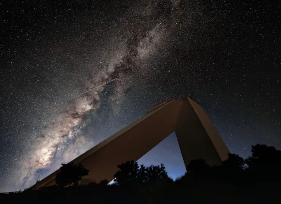 the McMath-Pierce Solar Telescope building set against the backdrop of the Milky Way and a meteor (or shooting star) streaking across the sky.