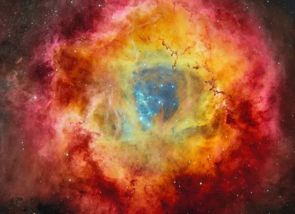 Stars on a dark blue background surrounded by clouds of a yellow, red and magenta nebula.