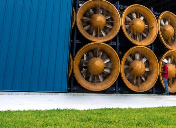 A bright blue hangar building containing an array of huge yellow fans.
