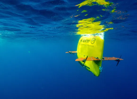 Underwater image of a bright yellow autonomous underwater vehicle in royal blue water.