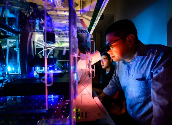 Researchers look into a microscope in a darkened room.