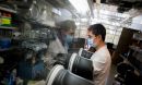 A man in a lab working on something behind a protective glass shield.