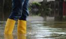 A person wearing yellow boots stands in flood water.