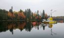 A yellow platform with solar panels and other equipment on it floating on a still lake with trees showing fall colors in the background.