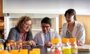Three scientists wearing safety glasses in a lab with test bottles in the foreground
