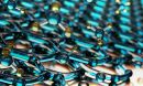 Two layers of a lattice of translucent blue beads connected in hexagonal rings with some blue and yellow beads floating free from the matrix.