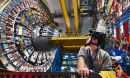 A researcher in a helmet looks up at a large ring of metal devices in the Large Hadron Collider.