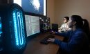 Two students work on computers while looking at a brightly lit screen.