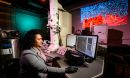 A researcher sits at a computer in a darkened lab.