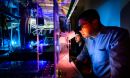 Researchers look into a microscope in a darkened room.