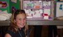 Young girl smiles at camera, science project in background.