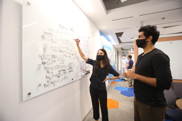 Two researchers stand at a white board that is covered in equations