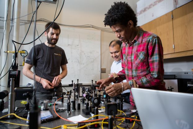 Three researchers stand around a work bench covered in research equipment