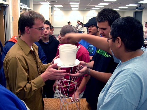 A group of students test the strength of a straw tower they built.