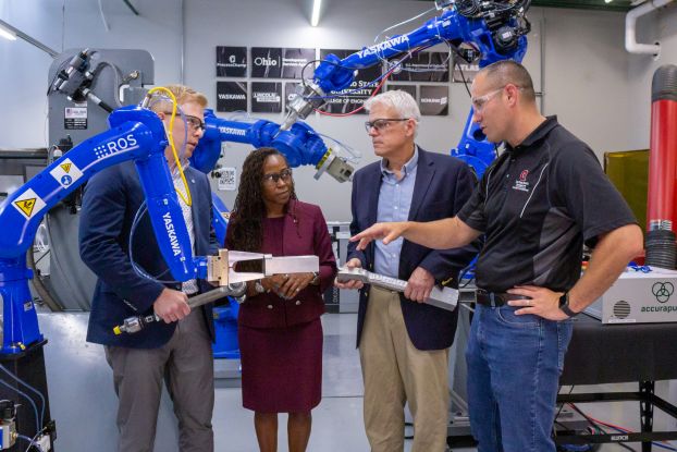 A group of people stand in a lab surrounded by robotic arms