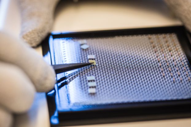 tweezers placing a computer chip on a screen.