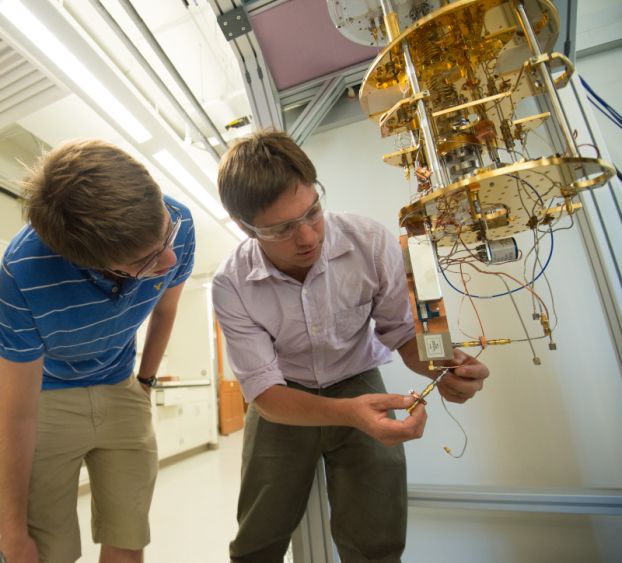 Two researchers work on a golden-colored piece of laboratory equipment.
