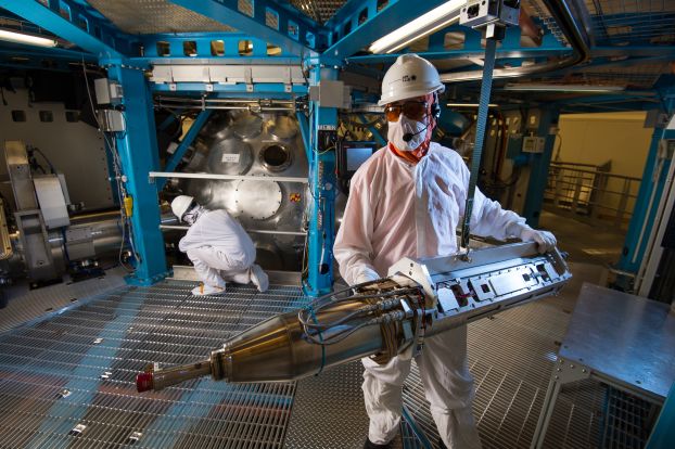 A technician wearing protective gear handles a large metalic cylinder.
