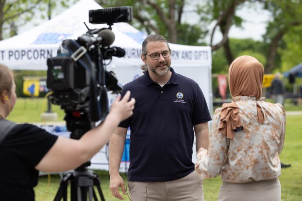 A man wearing a polo shirt with the NSF logo speaks to a reporter at an outreach event.