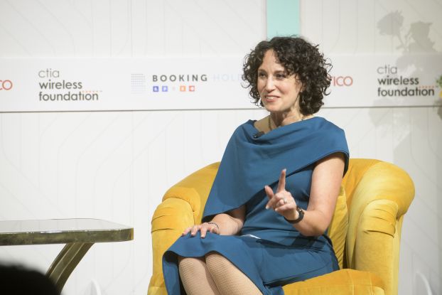 A woman in a dress sits on stage speaking at an event.