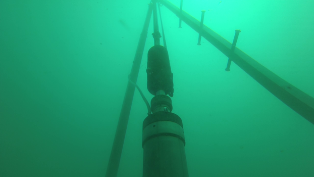 A drilling machine at the ocean's bottom surrounded the uniform greenish-blue of the ocean.