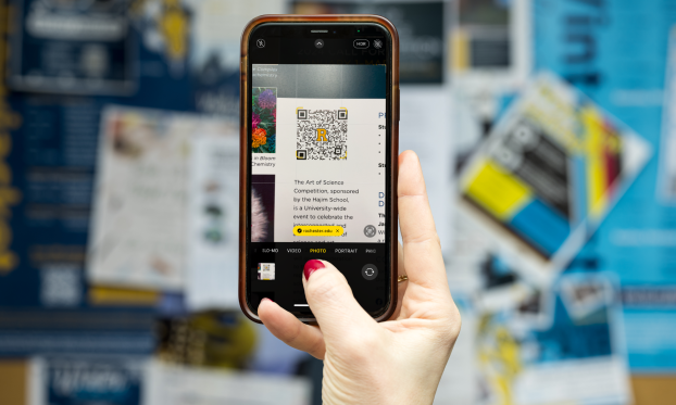 A hand holds a smartphone, which is displaying a QR code.