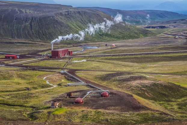 Steam rises from the chimney of a red building surrounded by the sparse Icelandic landscape.