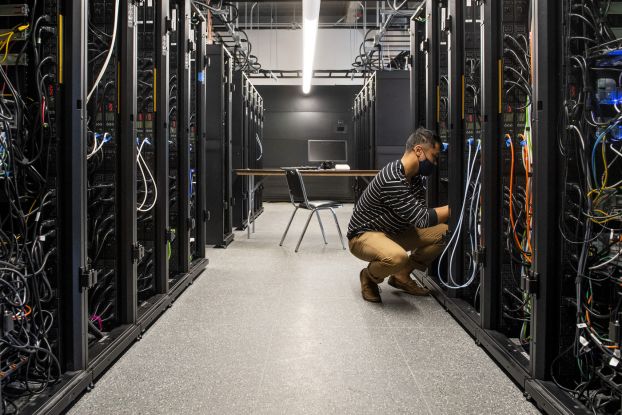 A person kneels in a server room as they work with various cables.