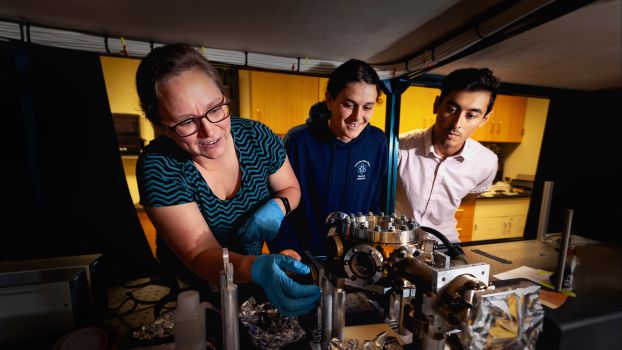 Three people leaning in to inspect a series of device components with various chambers metallic segments.