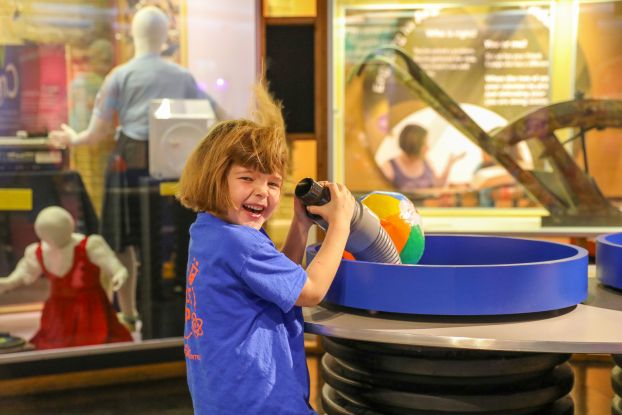 A young girl in a museum laughs as air blowing from a tube whips up her hair.