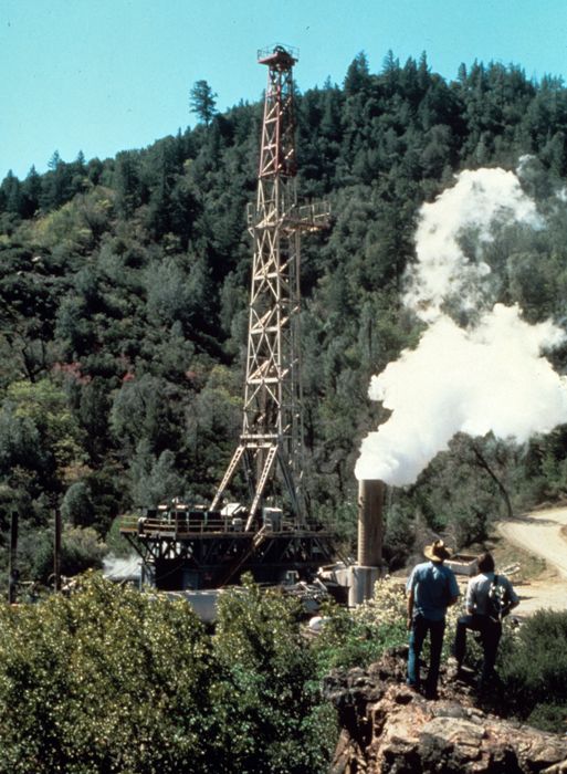 A 1970s-era photograph of a drilling tower in a mountainous region, accompanied by a steaming chimney.