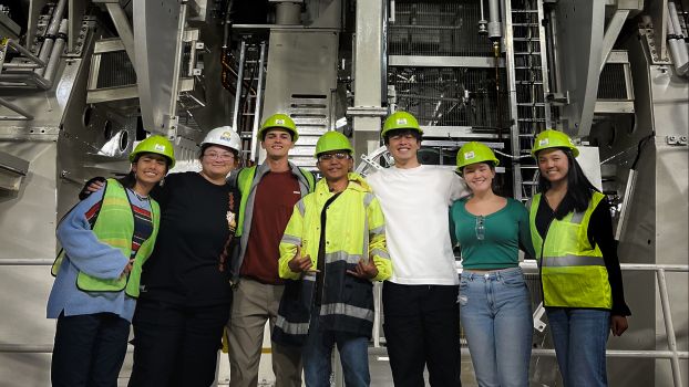 Group photo of students and mentors wearing hard hats in front of interior workings of the Inouye Solar Telescope facility