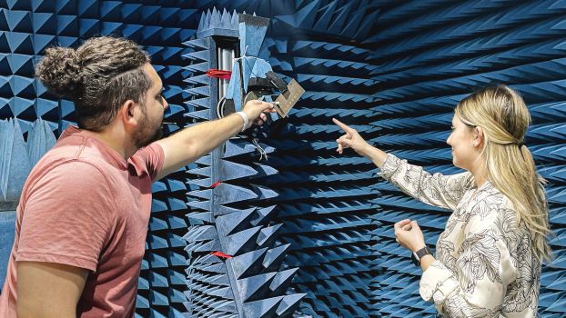 Two students working on an instrument in a room where the walls are covered in blue three-dimensional pyramid-shaped spikes.