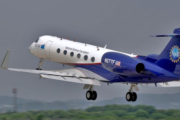 A blue and white jet with NSF and NCAR logos on it taking off.