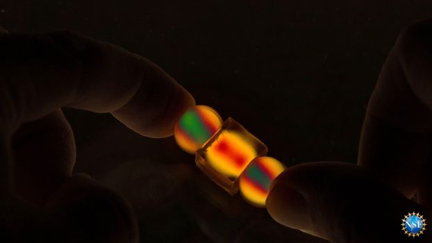 In darkness, thumbs hold two small spherical and one small cube objects that light up in vivid yellow, red, and green.