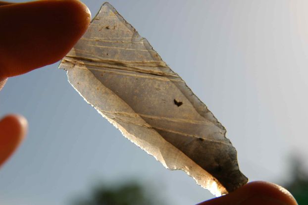 Fingers holding up an obsidian (volcanic glass) blade