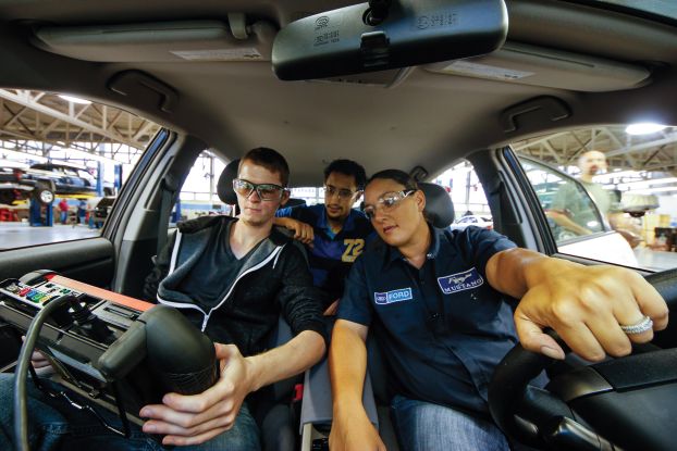 Three technicians sitting inside of a car, viewing a diagnostic screen.