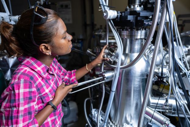 A student turns a knob on a large piece of metal equipment.