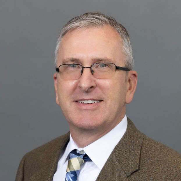 portrait of Timothy Patten, with grey hair, glasses, and wearing a brown suit
