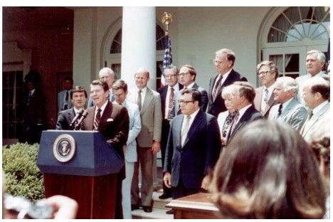 A photograph of President Reagan standing at a podium backed by members of Congress and the White House.